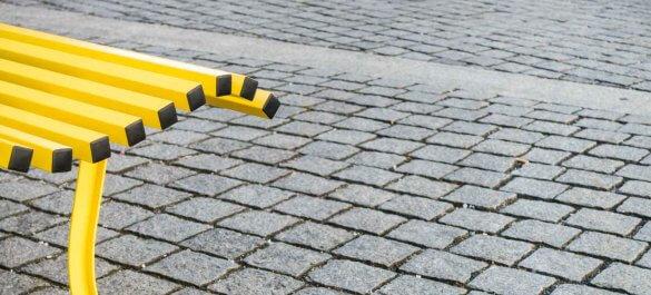 Gelbe Parkbank auf Pflastersteinen