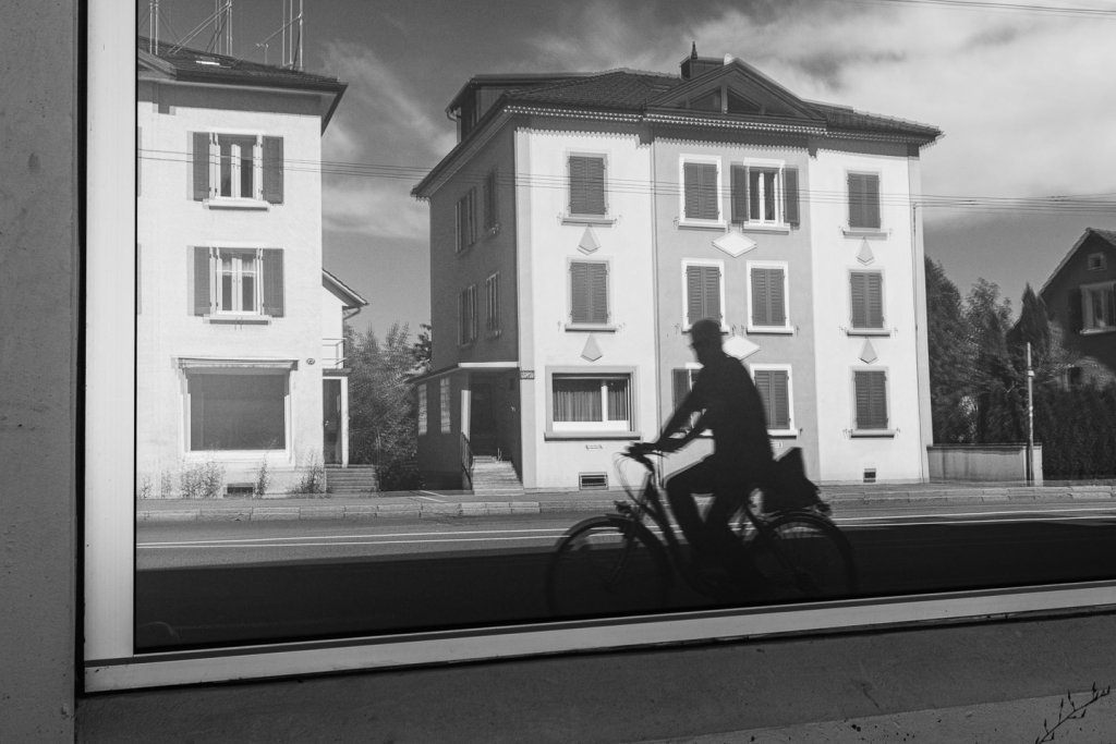 Zufälliger Radfahrer macht die Fensterspiegelung zum Bildmotiv Silhouette eines Radfahrers vor einer Fensterspiegelung mit Häuserfassaden