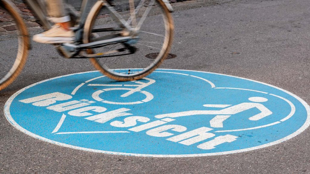 Geduld und der entscheidende Moment in der Schnappschussfotografie Velofahrer fährt über eine Strassenmarkierung mit dem Schriftzug Rücksicht