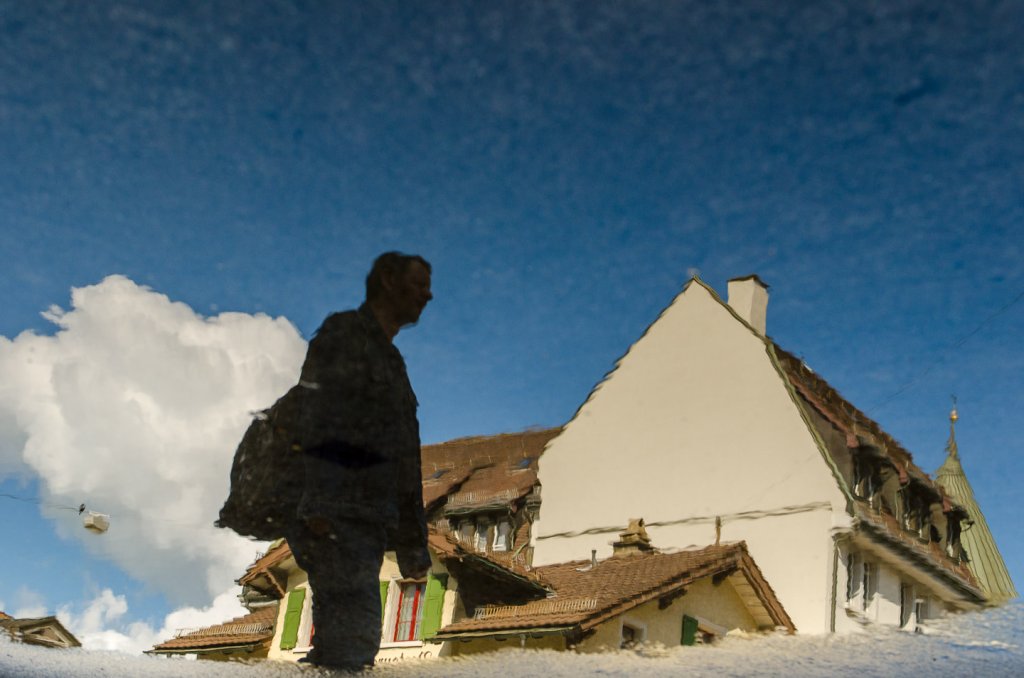 Der entscheidende Moment: Passant in einer Pfützenspiegelung Passant und Hausfassaden spiegeln sich in einer Pfütze