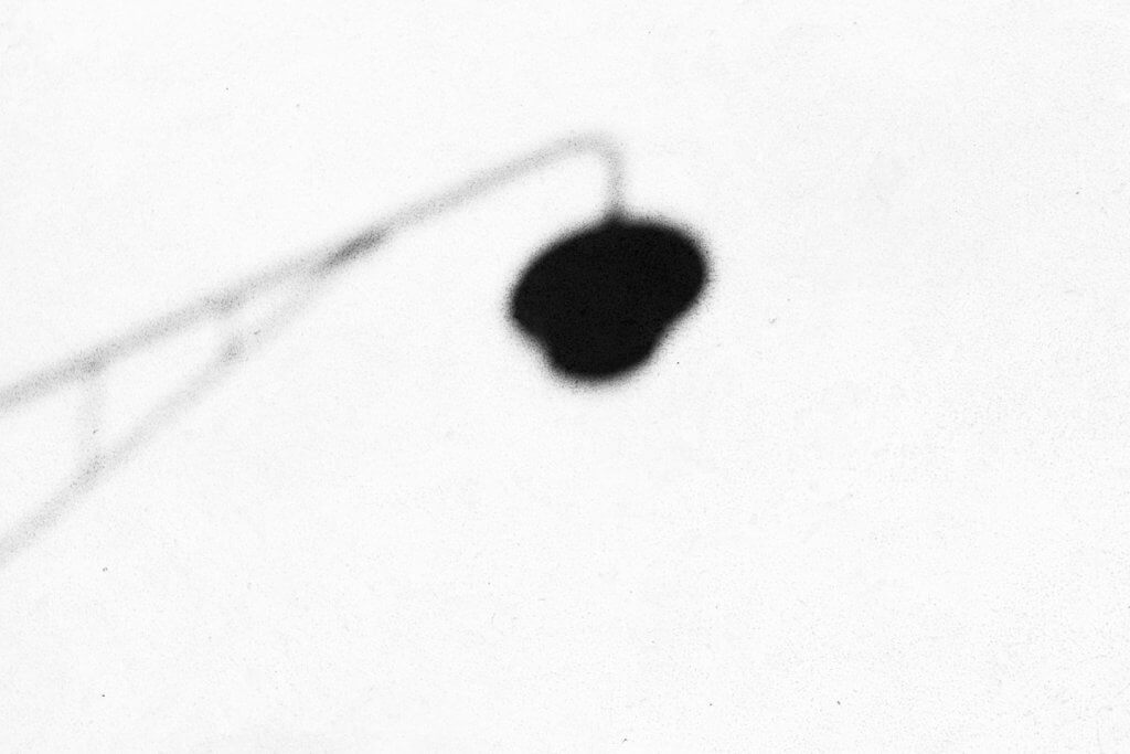 Minimalistische Schwarzweissfotografie mit Lampenschatten. Schatten einer Strassenlampe auf einer hellen Wand als minimalistisches Schwarzweissmotiv.